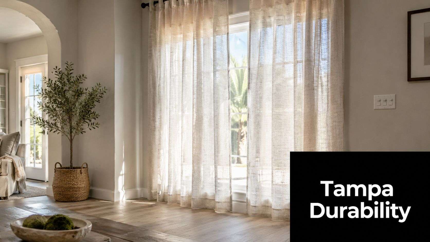 Sheer beige faux linen curtains hanging in front of a bright window with a decorative olive tree.