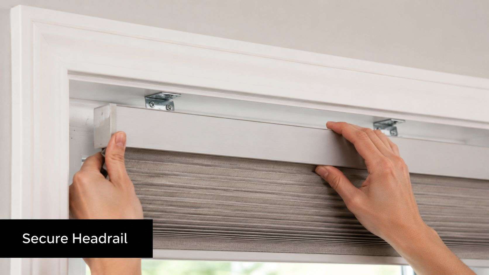 A person installing a gray cellular window shade by securing the headrail into the mounting brackets.