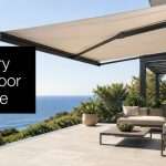 Black square sign reading 'Luxury Outdoor Shade' on a modern terrace overlooking the sea.