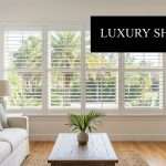 Bright living room with white plantation shutters on large windows, beige sofa with pastel cushions, and a wooden coffee table.