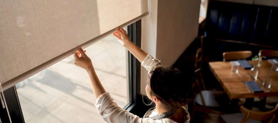 1787668673001_Hands-adjusting-roller-shade-in-restaurant | Drapery Company Hands adjusting roller shade in restaurant