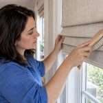 Homeowner dusting the folds of a Roman shade