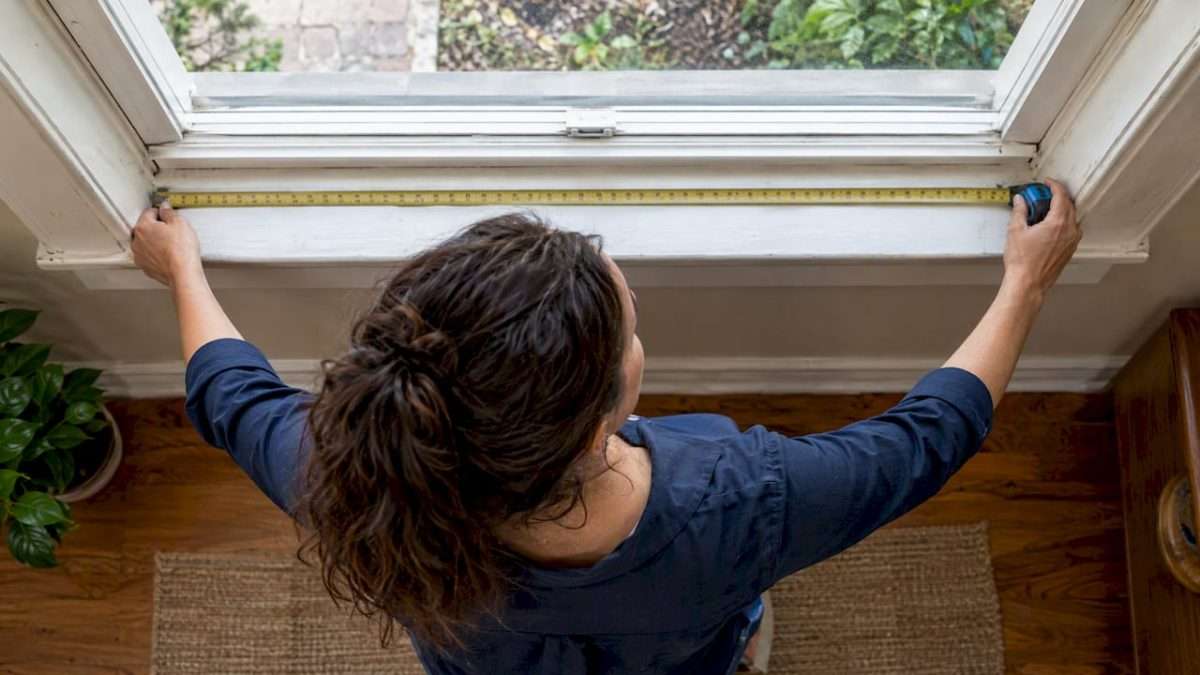 Homeowner measuring a window opening with tape