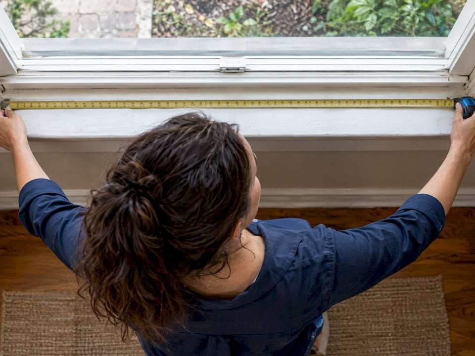 Homeowner measuring a window opening with tape