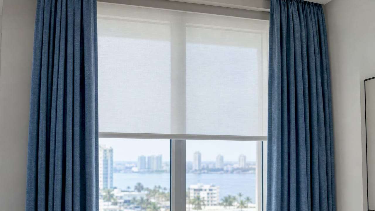 White window shade beneath lined blue drapery